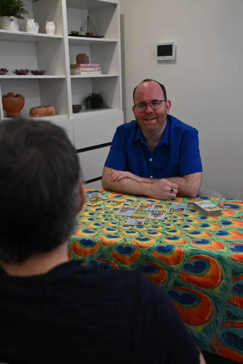 A tarot reading in progress across a peacock-feather tablecloth